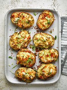 baked potatoes with cheese and seasoning on a white platter next to a napkin