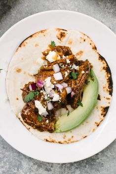 a tortilla topped with meat, onions and feta cheese on a white plate