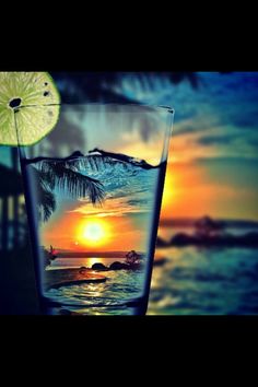 a lime slice sitting on top of a glass filled with water and an image of a sunset