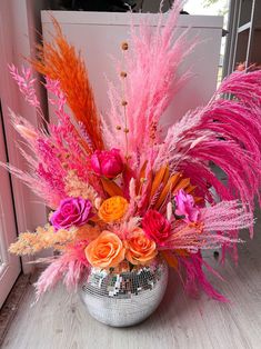 a vase filled with lots of different colored flowers and feathers on top of a wooden floor