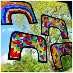 two colorful kites hanging from the side of a window with trees in the background