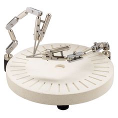 a clock made out of metal parts on top of a white surface with two hands holding the clock