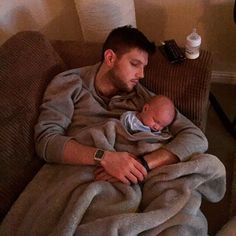 a man holding a baby wrapped in a blanket on top of a couch next to a remote control