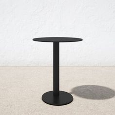 a black round table sitting on top of a cement floor next to a white wall