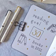 an open book with writing on it next to two pens and a notebook that reads reading goal 50 books in 2020