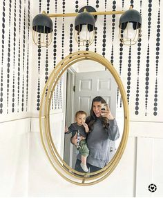 a woman holding a baby taking a selfie in front of a mirror with black and white wallpaper