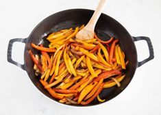 peppers being cooked in a skillet with a wooden spoon on the side and white marble counter top