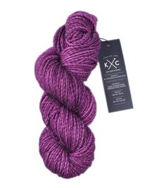 a skein of purple yarn next to a tag on a white background with a black and