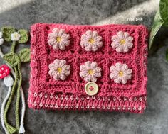 a pink crocheted purse with flowers on it and a green plant next to it