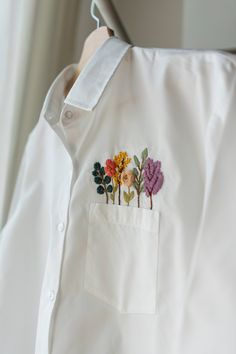 a white shirt with flowers embroidered on the front pocket and in the back pocket is a button down collar