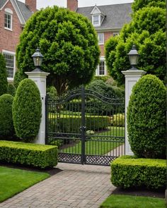 an iron gate surrounded by topiary hedges in front of a large brick house with white trimmings