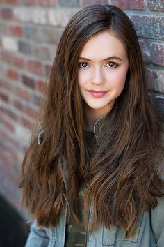 a young woman standing in front of a brick wall with her long hair pulled back