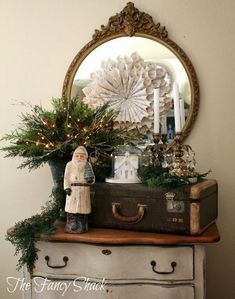 an old suitcase is sitting on top of a dresser with christmas decorations and greenery