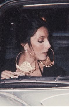 a woman sitting in the passenger seat of a car wearing large hoop earrings and looking at her phone