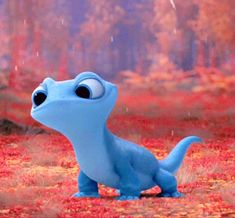 a blue toy with big eyes standing in the middle of an autumn forest filled with leaves