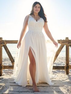 a woman in a white dress is standing on a wooden pier near the ocean and posing for a photo