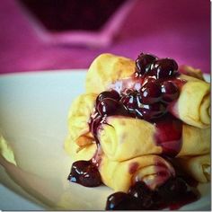 a white plate topped with crepes covered in blueberry sauce