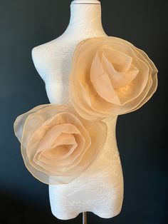 two white mannequins with beige fabric flowers on each one and a black background