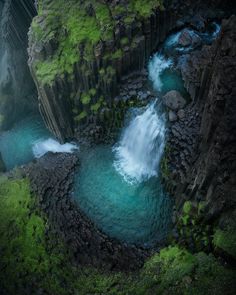 an aerial view of a waterfall in the middle of some rocks and green mossy vegetation