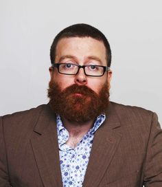 a man with glasses and a beard is posing for the camera while wearing a suit