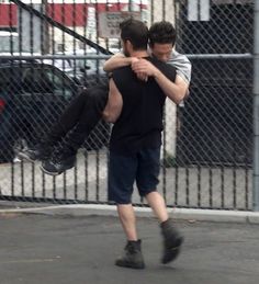 two men are playing with each other in front of a fenced area and cars