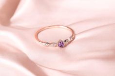 a close up of a ring on a pink satin material with diamonds and amethyst