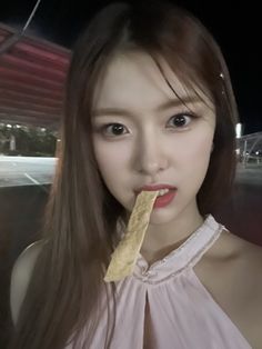 a woman with long hair holding a piece of food in her mouth and posing for the camera