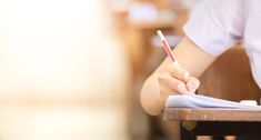 a person writing on a piece of paper with a red pen in their left hand