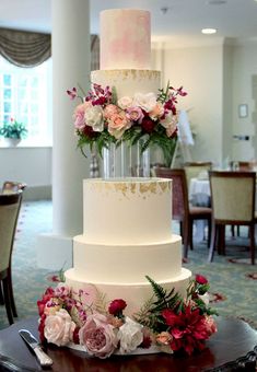 a three tiered wedding cake with pink and white flowers on the top is sitting on a table