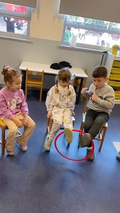 three children sitting on chairs in a classroom playing with a hula hoop around them