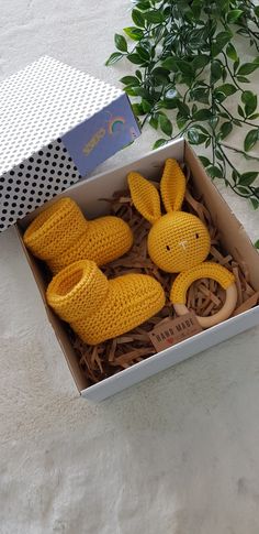 two yellow knitted rabbits in a box on a white surface next to some green plants