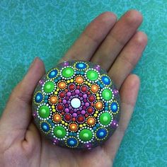 a hand holding a painted rock in the shape of a flower