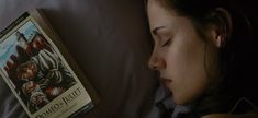 a woman laying in bed next to a book