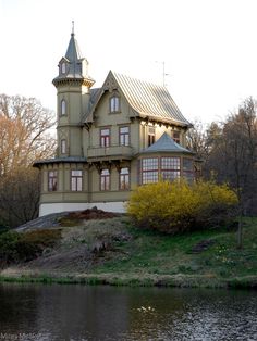 a large house sitting on top of a hill next to a body of water with trees in the background