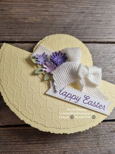 an easter card with purple flowers and a white bow on the front, sitting on a wooden surface