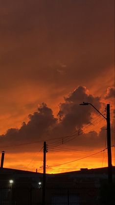 the sun is setting behind some power lines and telephone poles in front of an orange sky