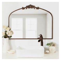 a white sink sitting under a large mirror next to a vase with flowers in it