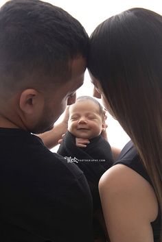 a man and woman holding a baby in front of their face while they are looking at each other