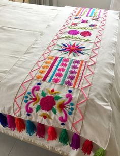 an embroidered table runner with colorful tassels and fringes on the edge, sitting on a bed