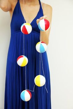 a woman in a blue dress is holding up some colorful balls and string attached to her head