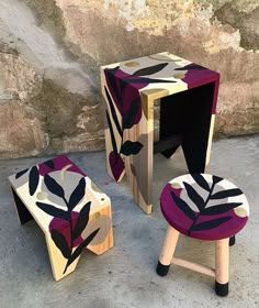 three stools and one table made out of wood with leaves painted on the sides