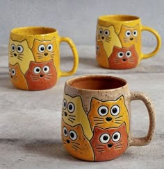 three yellow and orange mugs with cats painted on the inside, one has eyes