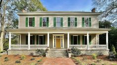 a white house with green shutters on the front porch and steps leading up to it