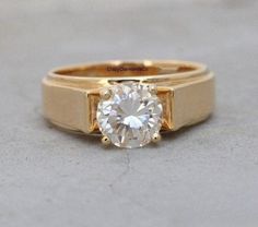 a yellow gold engagement ring with a round diamond in the center, on a gray surface