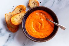 a bowl of tomato soup with some bread on the side and a spoon in it