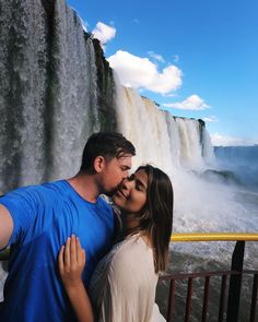 a man and woman kissing in front of a waterfall