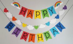 a happy birthday banner with rainbows and clouds hanging from the side of a wall