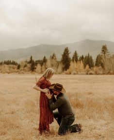 a man kneeling down next to a woman on top of a dry grass covered field