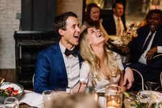 a man and woman sitting at a dinner table with their mouths open as they laugh