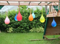 several colorful raindrops hanging from a wooden structure in front of a green yard